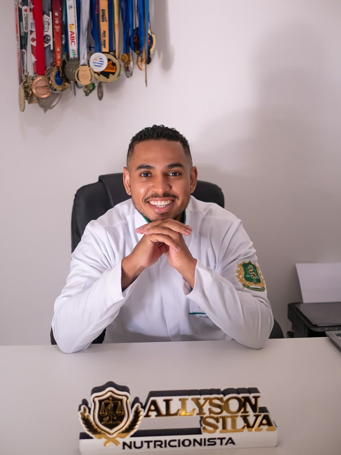 Nutricionista Allyson Silva sorrindo em seu consultório, de jaleco branco